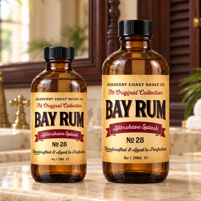 Barberry Coast Bay Rum No. 28 Aftershave Splash in 4 oz and larger 8 oz amber bottles with vintage yellow labels, side by side on a cream marble countertop in a British Colonial bathroom with dark wood, brass fixtures and tropical greenery.
