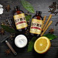 Bay Rum Aftershave Splash, Balm/Lotion, Shave Soap, Muhle Double Edge Safety Razor, Shaving Brush Flatlay Photo on a wood background with ingredients scattered around the products (bay leaves (Pimenta Racemosa), vanilla beans, clove, orange, allspice berries).