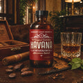A bottle of Barberry Coast Shave Co. Havana Aftershave Splash stands on a rustic wooden table, surrounded by a cigar, an open wooden box, a glass of amber liquid, coffee beans, and dried leaves.