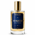 A 100ml bottle of Morocco Extrait Reserve fragrance by Barberry Coast Fine Fragrances. The clear glass bottle displays a golden-amber liquid, topped with a metallic gold cap and featuring a dark blue label with gold lettering.